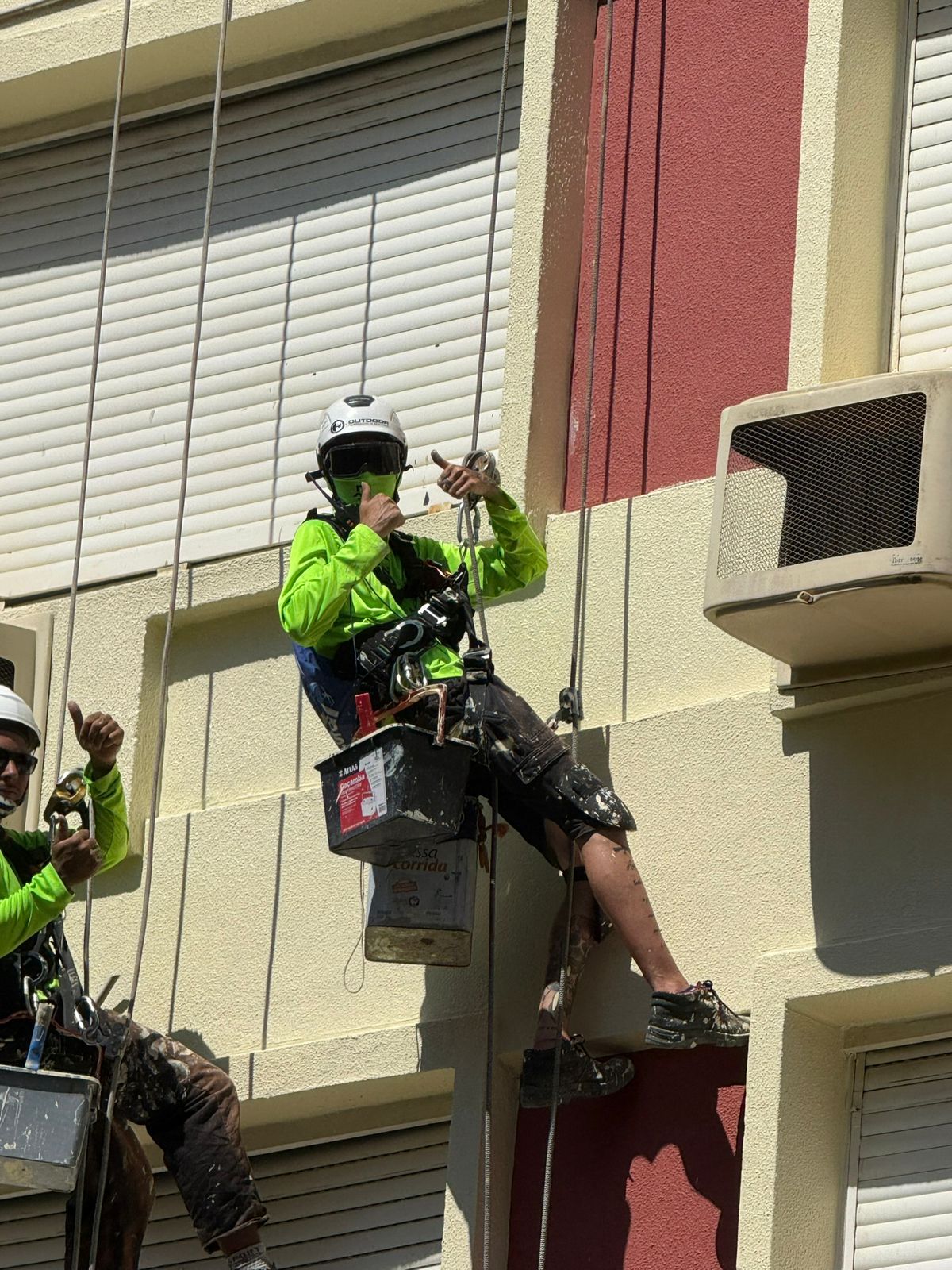 Profissional em rapel pintando fachada de prédio