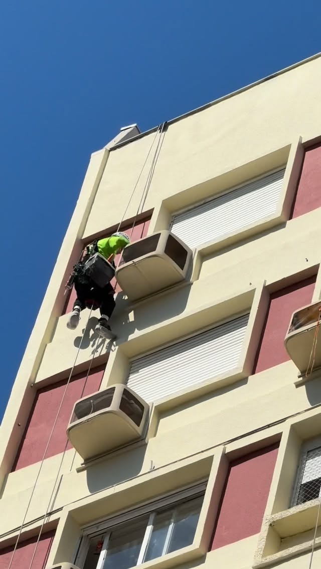 Profissional em rapel realizando pintura externa